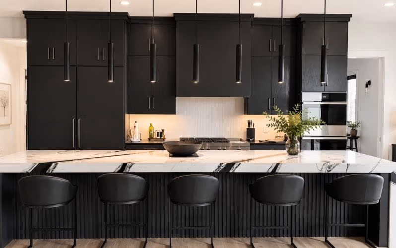 Modern kitchen with black cabinetry, marble island, black stools, and hanging pendant lights.